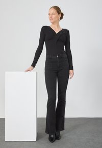 Fekete, hosszú ujjú, v-nyakú bodysuit, csavart elülső dizájnnal, magas derékú fekete, trapéz farmernadrággal és fekete magassarkú csizmával párosítva.