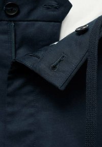 Jachetă bleumarin dintr-un material texturat, cu închidere cu nasturi, guler cusut și detalii cu buzunare cu fermoar pe laterale.