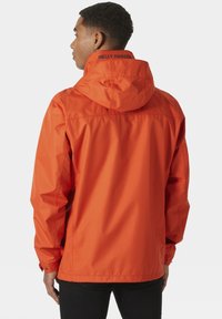 Chaqueta impermeable de color naranja brillante con capucha, puños elásticos y detalles de logotipo negro en la parte posterior. Material suave y liviano.