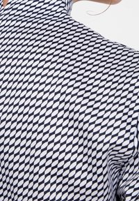 Skjorta med krage som har ett geometriskt diamantsmönster i marinblått och vitt. Tyget verkar slätt med en lätt glans som framhäver strukturen.