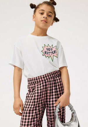 Vit t-shirt med kort ärm och en grafisk text "DU ÄR VIKTIG!" i rosa och grönt. Matchas med svart och rosa rutig byxa, hållandes en silverväska.