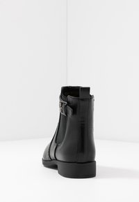 Stivale alla caviglia in pelle nera con pannelli laterali elasticizzati, una cintura decorativa e fibbia, texture liscia e tacco basso a blocco.