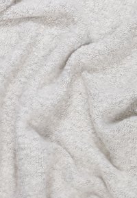 Couverture douce et texturée en gris clair avec un aspect pelucheux et duveteux. Le matériau semble épais et confortable, avec des motifs subtils tout au long.