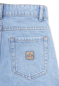 Vaaleansinisiä farkkuja, joissa on takatasku, jossa on neliömäinen paikka, jossa lukee "B/R" mustalla beigellä taustalla. Teksturoitu kangas, jossa on hieno haalistuminen.