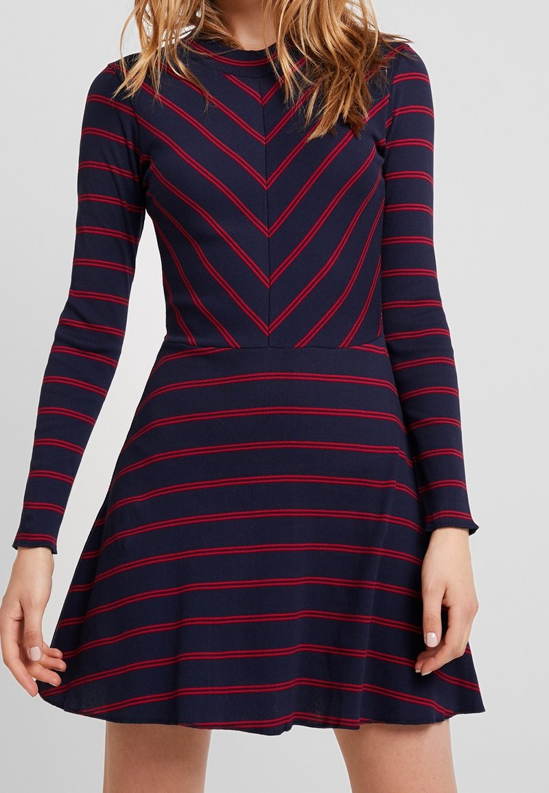 Abito lungo blu navy a maniche lunghe con righe orizzontali rosse. Corpino aderente con motivo a zig zag; gonna a ruota. Tessuto morbido, stile casual.