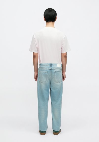 Ροζ ανοιχτόχρωμο μπλουζάκι με κοντά μανίκια, άνετο ανοιχτό μπλε τζιν παντελόνι με λευκή μέση και πράσινα παπούτσια με καφέ σόλες.