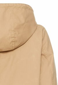 Hellbeige Kapuzenjacke mit glatter Textur und sichtbaren Nähten. Sie hat ein einfaches Design, das sich auf Funktionalität und Komfort konzentriert.