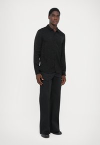 Black long-sleeve shirt with a textured pattern, paired with wide-leg black trousers. The ensemble features a modern silhouette and subtle detailing.