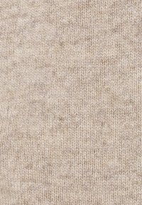 Beige stickat tyg med en mjuk textur, som har ett subtilt melerat mönster och jämna sömmar, vilket ger ett varmt och neutralt utseende.