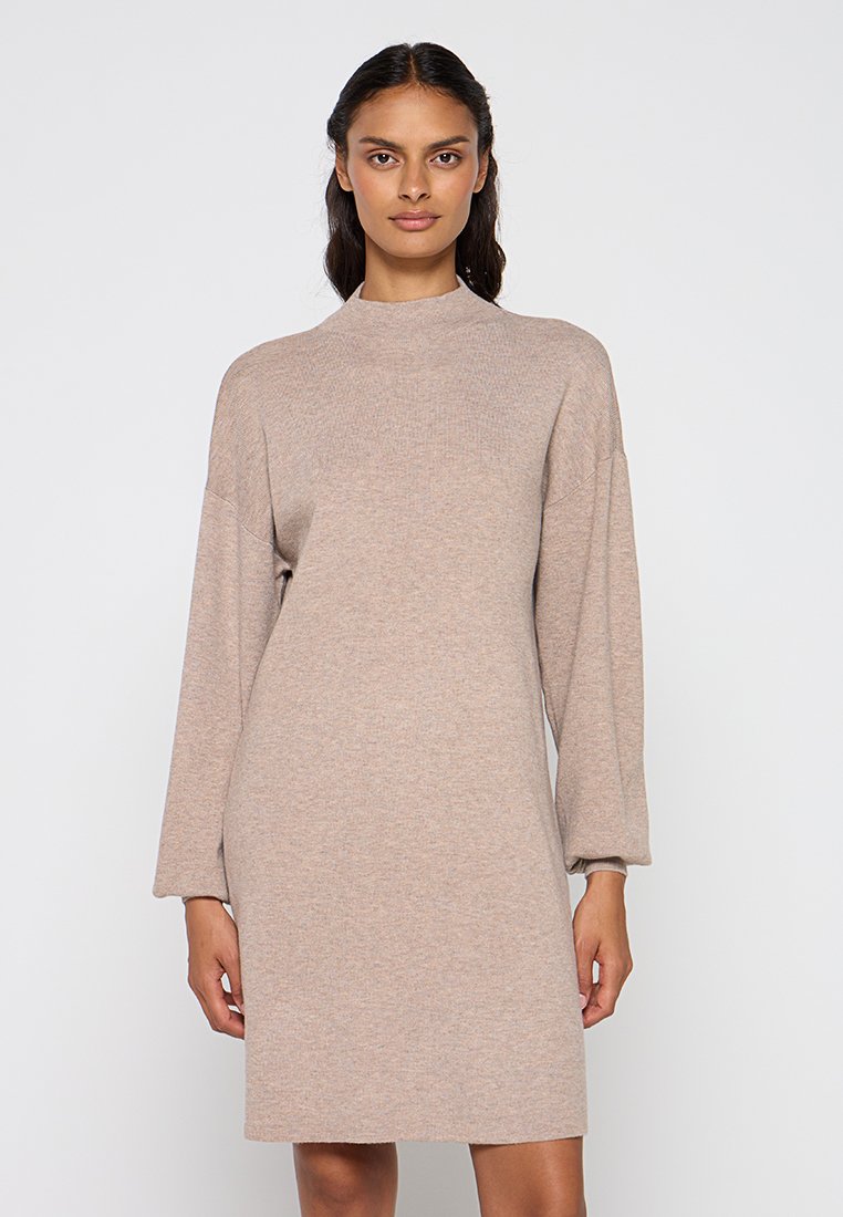 Robe en tricot beige, longueur genoux, avec un col haut et des manches longues, légèrement bouffantes. Texture douce et coupe décontractée.