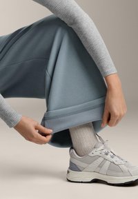 Svetlomodré voľné tepláky s rebrovanými manžetami, v kombinácii so svetlosivým rebrovaným dlhým rukávom a sivými atletickými topánkami s sieťovinovými akcentmi.