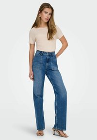 Jeansy z wysokim stanem w niebieskim odcieniu denim, prostą nogawką, z dwoma przednimi kieszeniami oraz jasnobeżową, prążkowaną bluzką z krótkim rękawem.