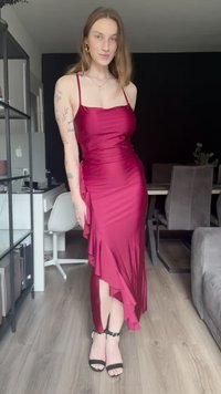 Bordová saténová šaty s tenkými ramienkami, riaseným detailom na strane a asymetrickým lemom, skombinované s čiernymi sandálmi na vysokom podpätku na drevenej podlahe.