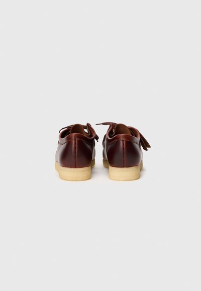 Zapatos de cuero marrón con un diseño redondeado, que cuentan con una suela de goma de color claro en contraste y cordones en la parte trasera.