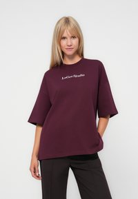 Burgundy oversized t-shirt with short sleeves, featuring white “LeGer Studio” logo on the front. Soft cotton material, relaxed fit.