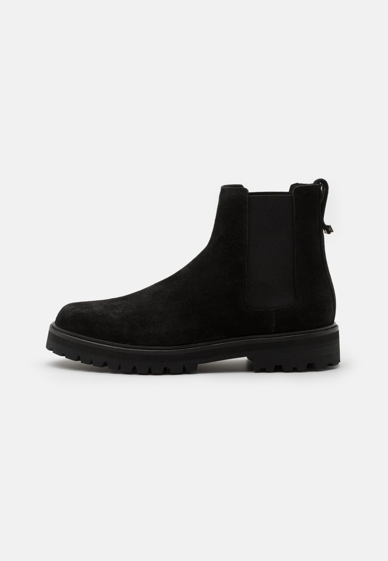 Botte Chelsea en daim noir avec panneaux latéraux élastiques, languette au talon et semelle extérieure épaisse en caoutchouc à crampons, vue de profil droit sur fond blanc.