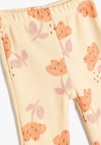Ribmede leggings i en lys gul farve med et blomster mønster, der har fersken og lyserøde blomster, accentueret af brune prikker.