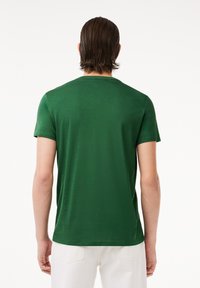 T-shirt verde in cotone con maniche corte, collo rotondo e texture liscia. Vista da dietro. Design minimalista senza motivi.