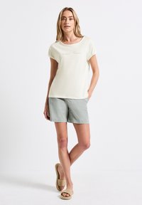 Ljusgrön kortärmad topp med texten "SOMMAREVENINGAR", kombinerad med ljusgröna shorts och beige vävda slip-on sandaler.