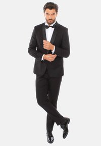 Tuxedo nero con rever in satin, camicia bianca e papillon nero. Design aderente, tessuto liscio, abbinato a scarpe eleganti nere lucide.