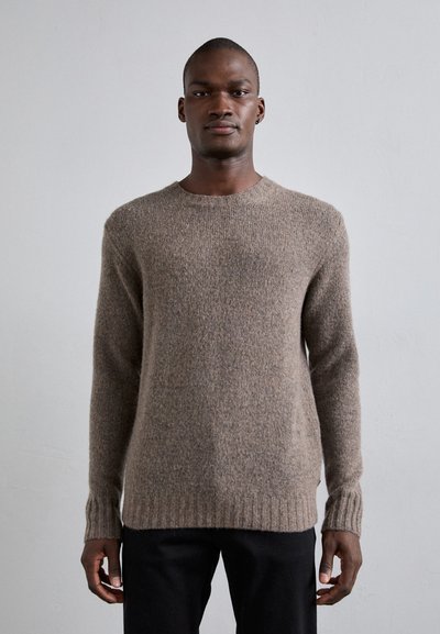 Suéter de punto marrón con cuello redondo, puños y dobladillo acanalados, que presenta una textura suave y un tejido de peso medio. Llevado con pantalones oscuros.