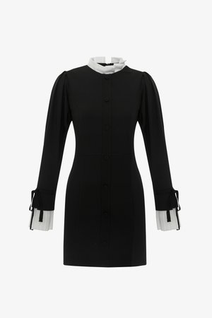 Robe noire avec un col blanc haut, fermeture à boutons sur le devant et manches longues dotées de poignets plissés blancs avec des liens. Texture de tissu lisse.