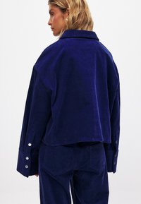 Navy corduroy jacket with a loose fit, wide collar, and buttoned cuffs. Textured fabric with vertical ribs and a clean finish.