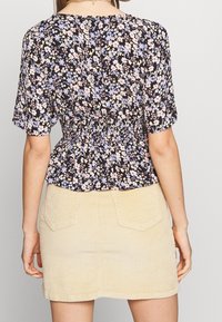 Blusa floreale con sfondo nero, maniche corte e vita arricciata, abbinata a una mini gonna in corduroy beige chiaro con tasche posteriori.
