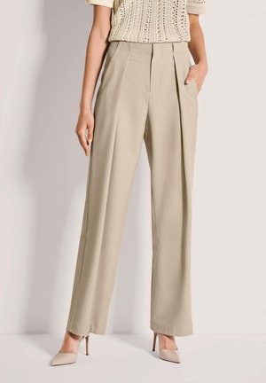 Beige plissierte Hosen aus leichtem Stoff, mit hohem Bund und zwei Seitentaschen. Kombiniert mit nude-farbenen High-Heels.