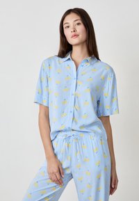 Lichtblauwe gestreepte pyjama's met een geel fruitpatroon, korte mouwen overhemd met knopen en bijpassende broek met elastische taille. Zachte stofstructuur.
