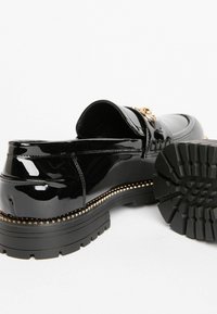 Mustad lakknahkstest loafers paksu kummitallaga ja kuldse detailiga. Omab siledat tekstuuri ja ümarat kuju.