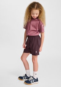 Mörkröd kortärmad skjorta och mörka shorts med elastisk midja. Barnet har på sig marinblå sneakers med vita detaljer och strukturerade vita strumpor.