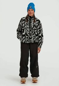 Black and white patterned fleece jacket with a half-zip front, paired with black pants and a blue knit beanie. Features an emblem on the chest.