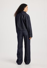 Donkerblauwe corduroy jas en bijpassende broek, met verticale strepen en een losse fit. De jas heeft een puntkraag en knoopdetails.