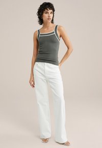 Grå figurnära linne med vit kant, kombinerat med vita utsvängda jeans. Modellen står mot en neutral bakgrund. Slät textur och modern design.