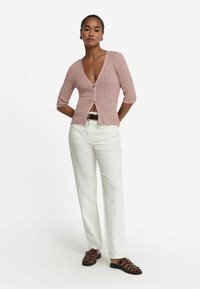 Rosa stickad cardigan med djup V-ringning, trekvartsärmar och knappar fram, i kombination med högmidjade vita byxor och bruna sandaler.