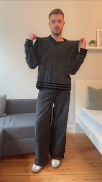 Gray cable-knit sweater with black striped cuffs and hem, paired with loose black pants and gray shoes, worn by a person standing indoors.