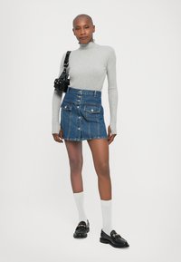 Pelēks garām piedurknēm turtlenecks top, apvienots ar zilu džinsūdenīšu svārku ar priekšējiem pogām un kabatām. Melni loafers un baltas zeķes papildina izskatu.