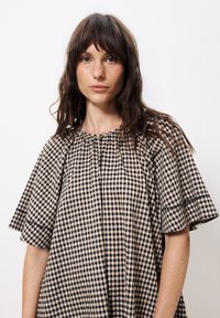 Kleid mit Gingham-Muster in Beige und Schwarz, ausgestattet mit kurzen Rüschensäumen, einem gerafften Ausschnitt und einer lockeren Passform.