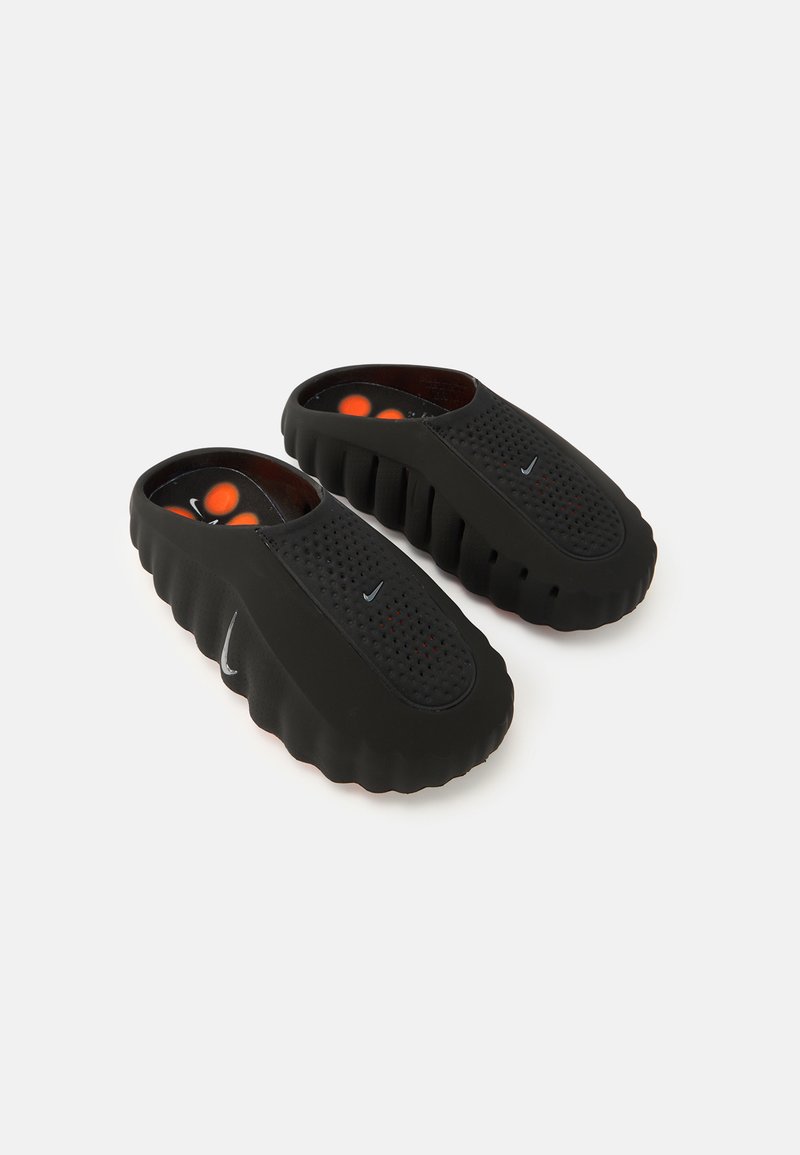 Μαύρα παπούτσια τύπου slip-on με υφή στο πάνω μέρος, διακοσμημένα με τρύπες, στρογγυλερή μύτη και παχύ, κυματιστό πέλμα. Ζωντανές λεπτομέρειες στο εσωτερικό.