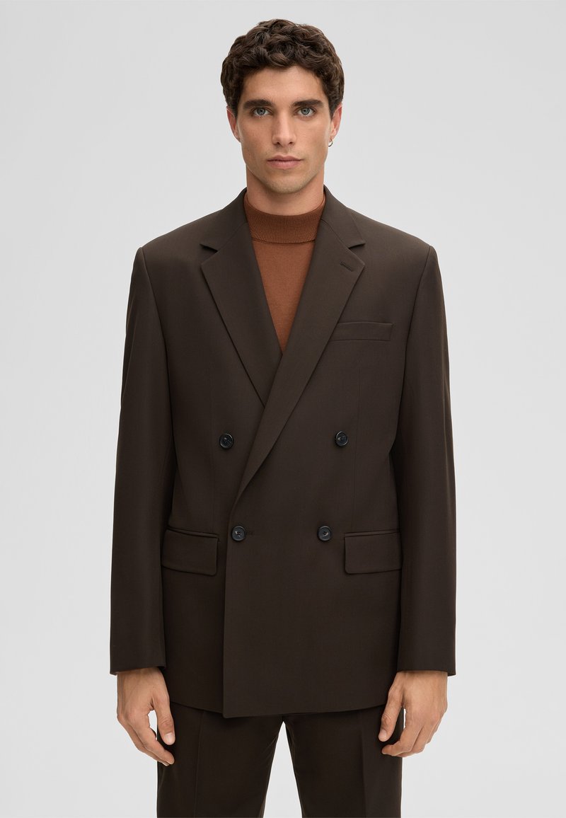 Bruine double-breasted blazer met grote zwarte knopen, ingesneden revers, voorzakken en een gladde textuur. Draagt over een bruine coltrui.