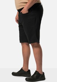 Pantalones cortos negros de algodón con un ajuste relajado, bolsillos y cierre con botón, combinados con zapatillas deportivas negras con acentos texturizados.