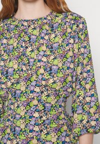 Gros plan d'une personne portant une robe fleurie avec des fleurs violettes, vertes, crème et bleues et des manches longues bouffantes.