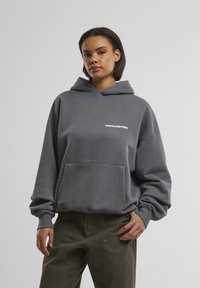 Grijze hoodie met een voorzak en de tekst "PROHIBITED" in het wit. Heeft een relaxte pasvorm en ribgebreide manchetten. Getextureerde stofafwerking.