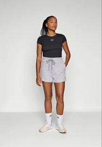Top nero aderente con logo, pantaloni corti grigi chiari con cordoncino, calze bianche a cuffia e scarpe da ginnastica beige con dettagli. Tessuto liscio; design casual.