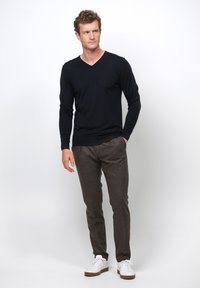 Marinblå V-ringad långärmad tröja i kombination med bruna byxor och vita sneakers; slät textur, figurnära design och avslappnad hållning.