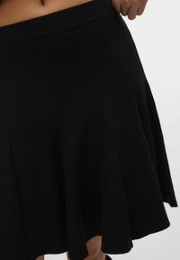 Jupe noire évasée avec une taille côtelée et un design plissé, fabriquée à partir d'un matériau doux avec une texture lisse.