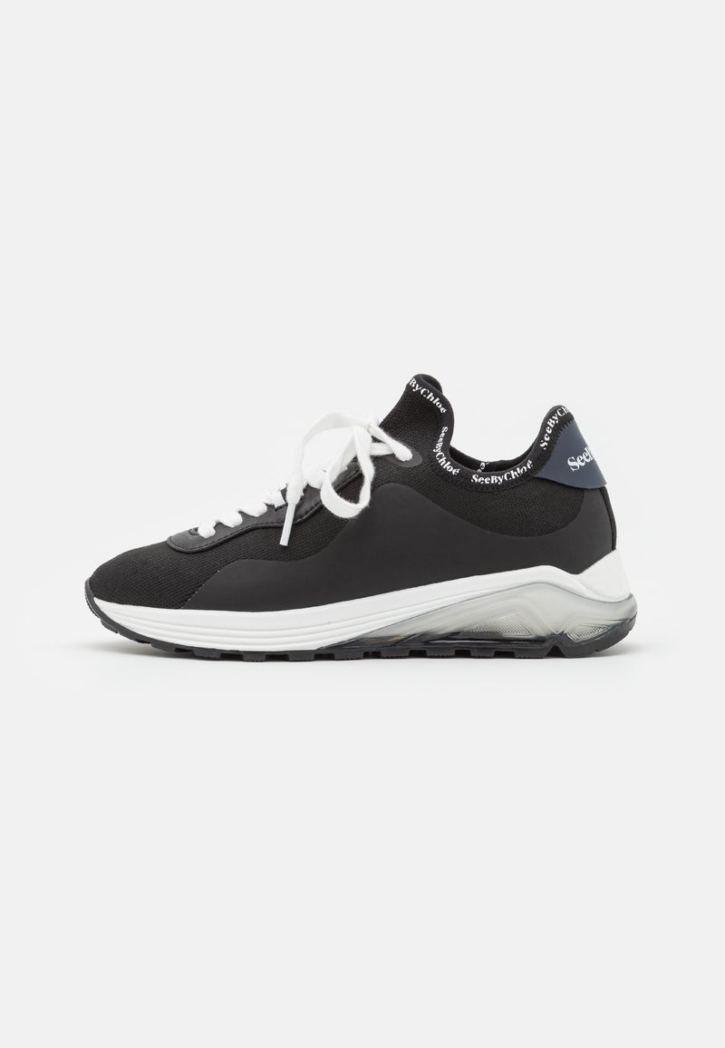 Zwarte sportieve schoenen met een gestructureerde bovenkant, witte veters en een contrasterende zool. Heeft een logo op de hiel en een gebogen ontwerp voor ondersteuning.
