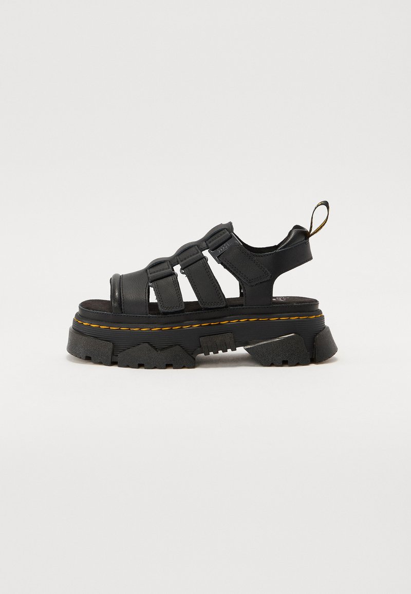 Black platform sandal made of synthetic material, featuring three adjustable straps, a textured sole, and contrasting yellow stitching.