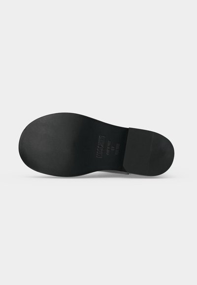 Semelle de chaussure en cuir noir avec talon et texte de marque embossé sur un fond gris clair uni.